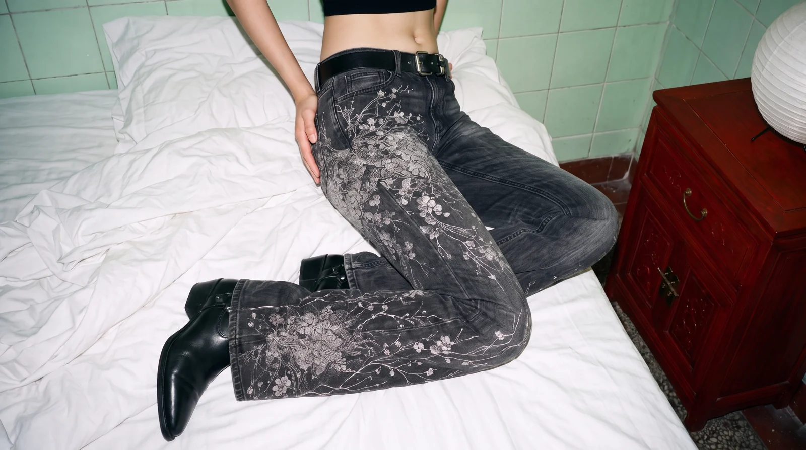 K02 YUN low rise wide leg jean, kneeling on a bed, washed black denim with a laser-etched plum blossom
