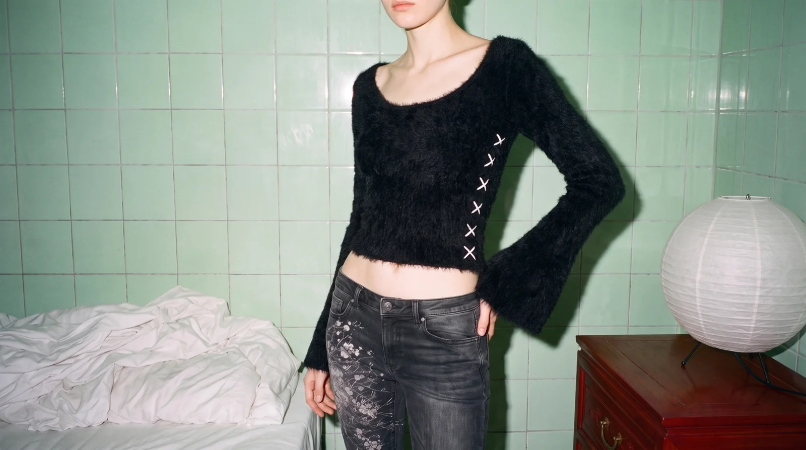 K05 CHA mohair top in black with white X stitches, standing against green tiles